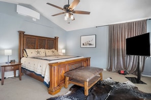 A bedroom with a wooden bed, a ceiling fan, a mounted TV, a bedside table, and a large rug. - Indian Springs | 4BR Lakehouse w/ Fishing & BBQ (Bandera)