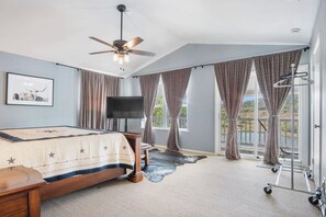 A bedroom with a bed, a ceiling fan, a TV, and a view of the outdoors.