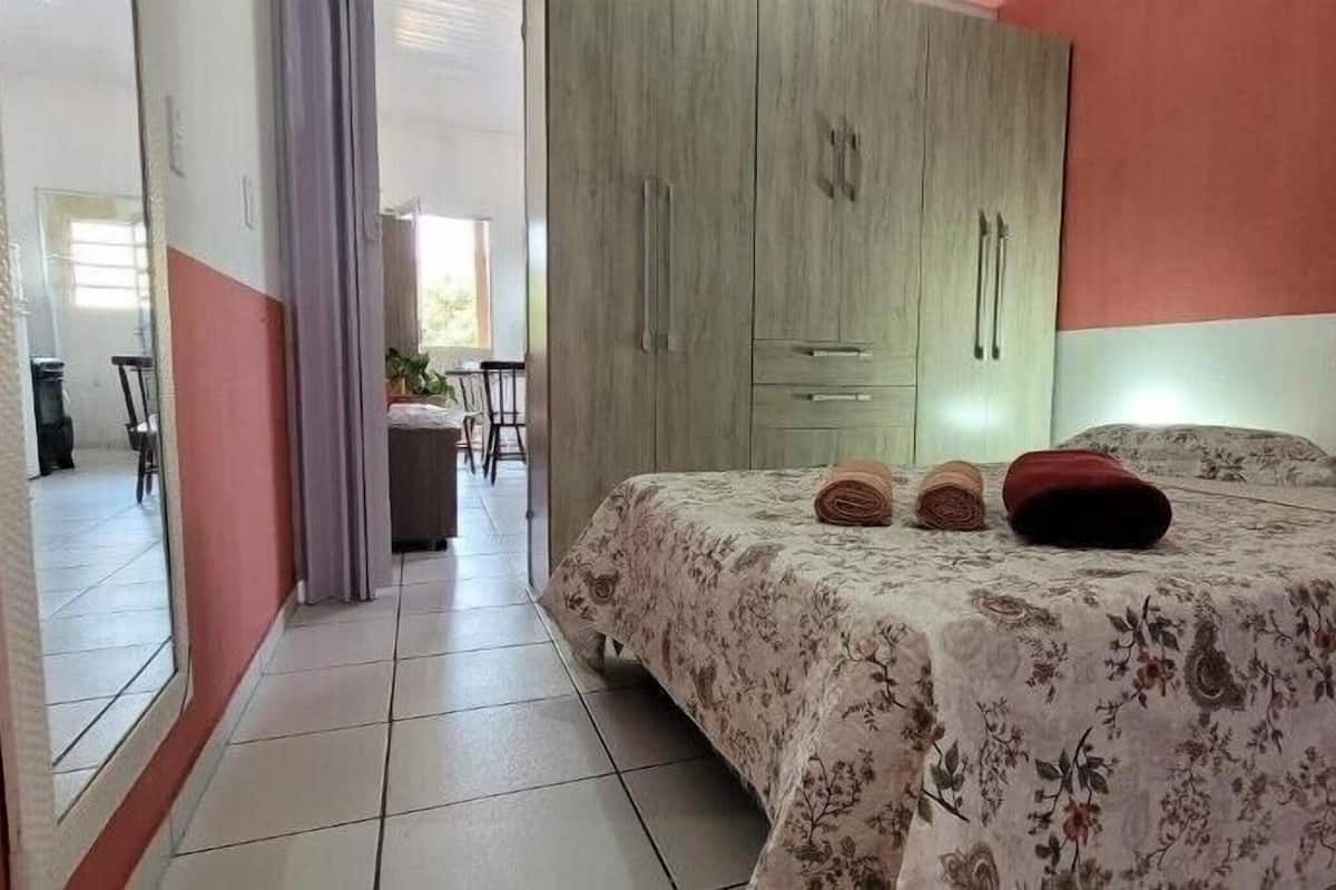 A bedroom with a bed, a wardrobe, and a view of a dining area.