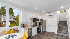 A modern kitchen with white cabinets, stainless steel appliances, and a dining area with yellow chairs. - The Golden Lion Sweet Suite (Seattle)