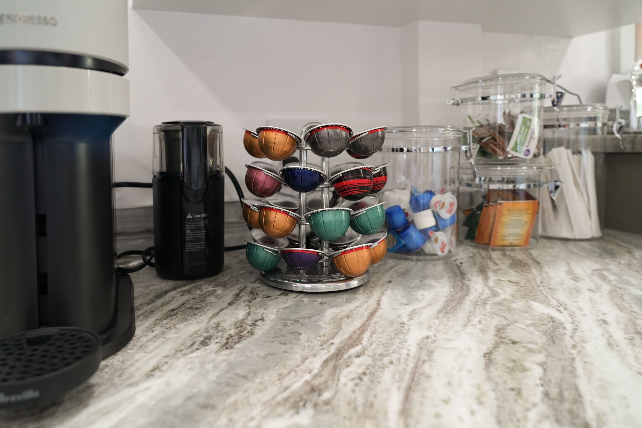 A kitchen counter with a coffee maker, a coffee pod holder, and a spice rack.