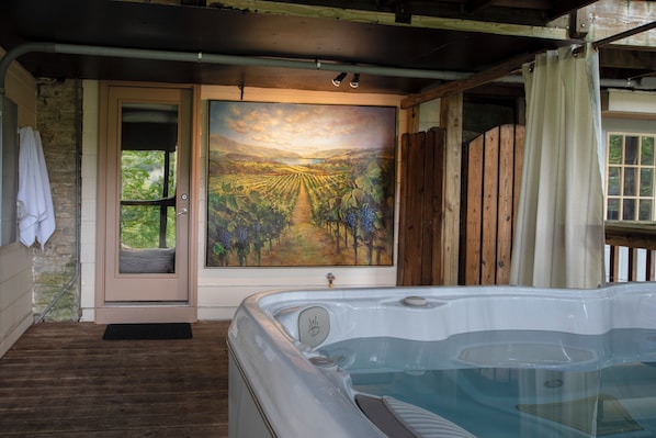 A hot tub with a view of a vineyard, a wooden door, and a stone wall.