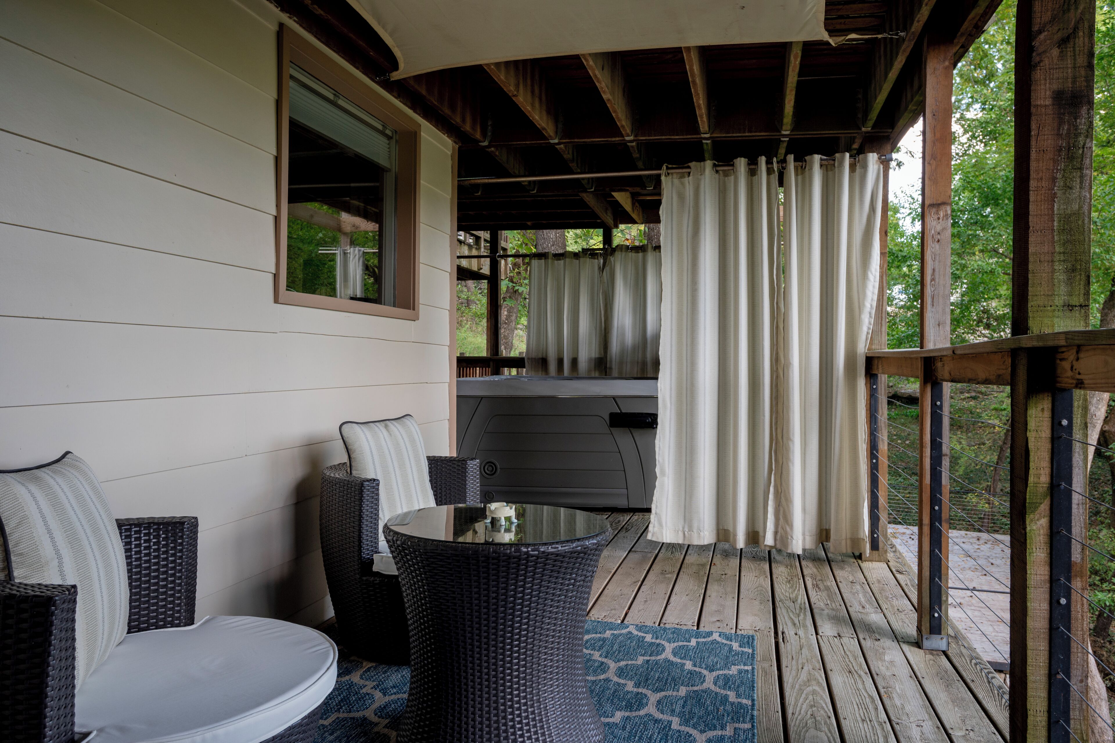 A covered outdoor seating area with wicker furniture, a table, and a view of a hot tub.