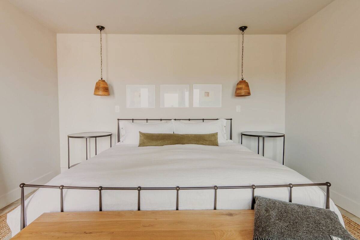 A bedroom with a large bed, bedside tables, a wooden bench, and pendant lights.