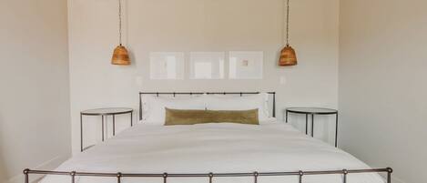 A bedroom with a large bed, bedside tables, a wooden bench, and pendant lights.