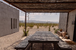 An outdoor patio with a concrete table and benches, surrounded by desert vegetation and mountains in the background.