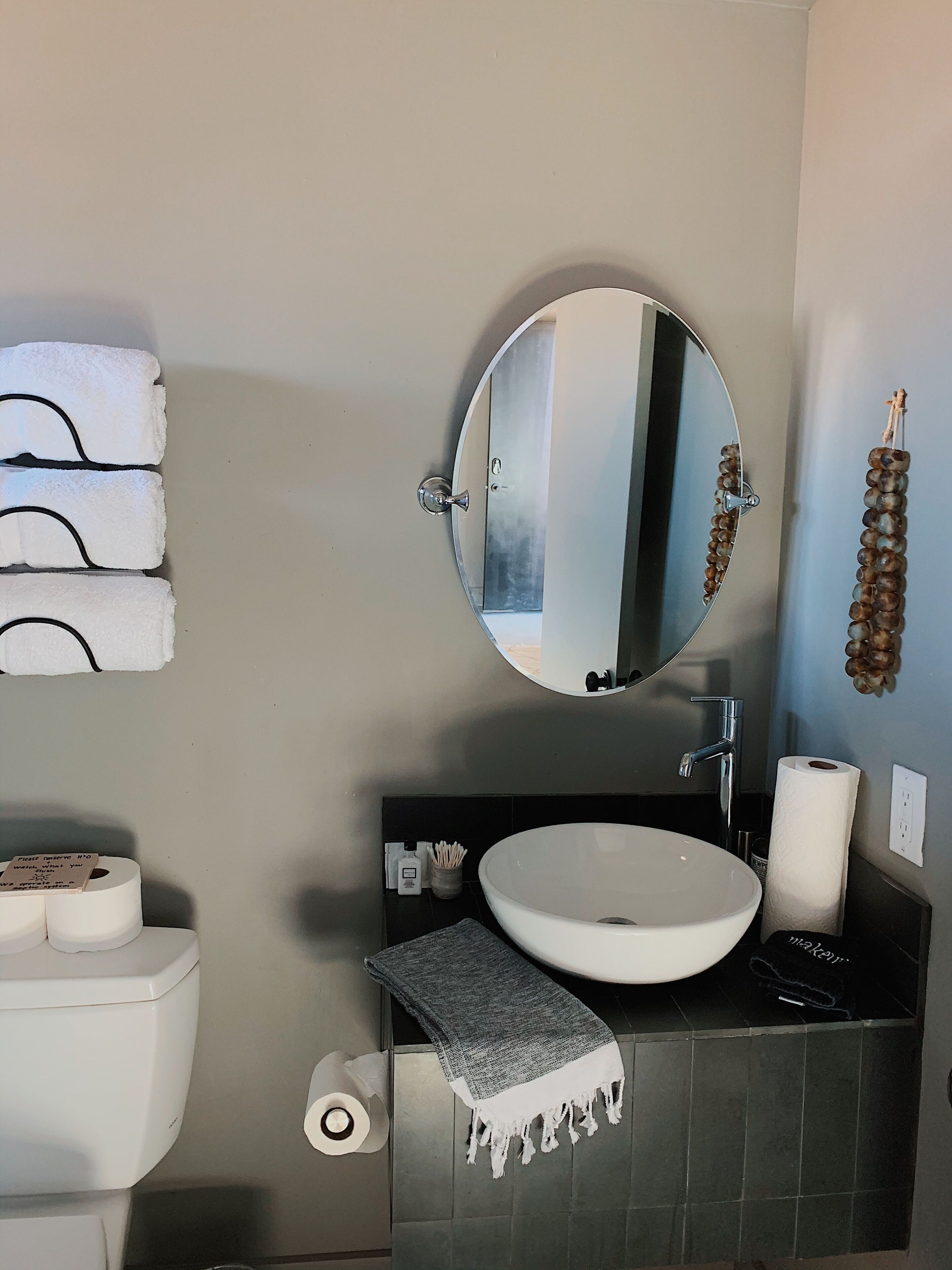 Un baño con un espejo redondo, un lavabo blanco y un perchero para toallas.