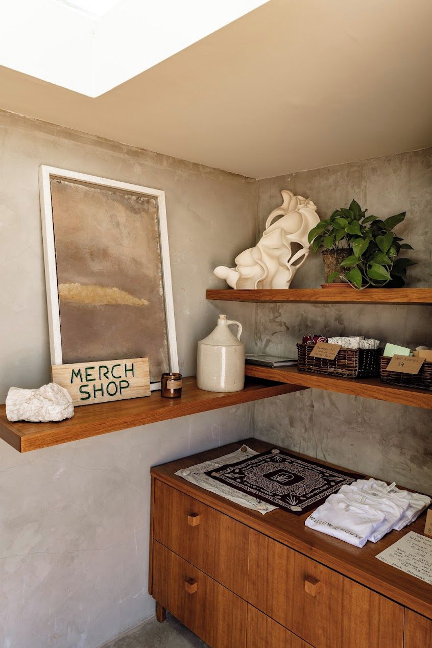 Une pièce comprenant une commode en bois, une œuvre d’art encadrée, une étagère avec des objets décoratifs et un panneau indiquant « BOUTIQUE DE PRODUITS DÉRIVÉS ».