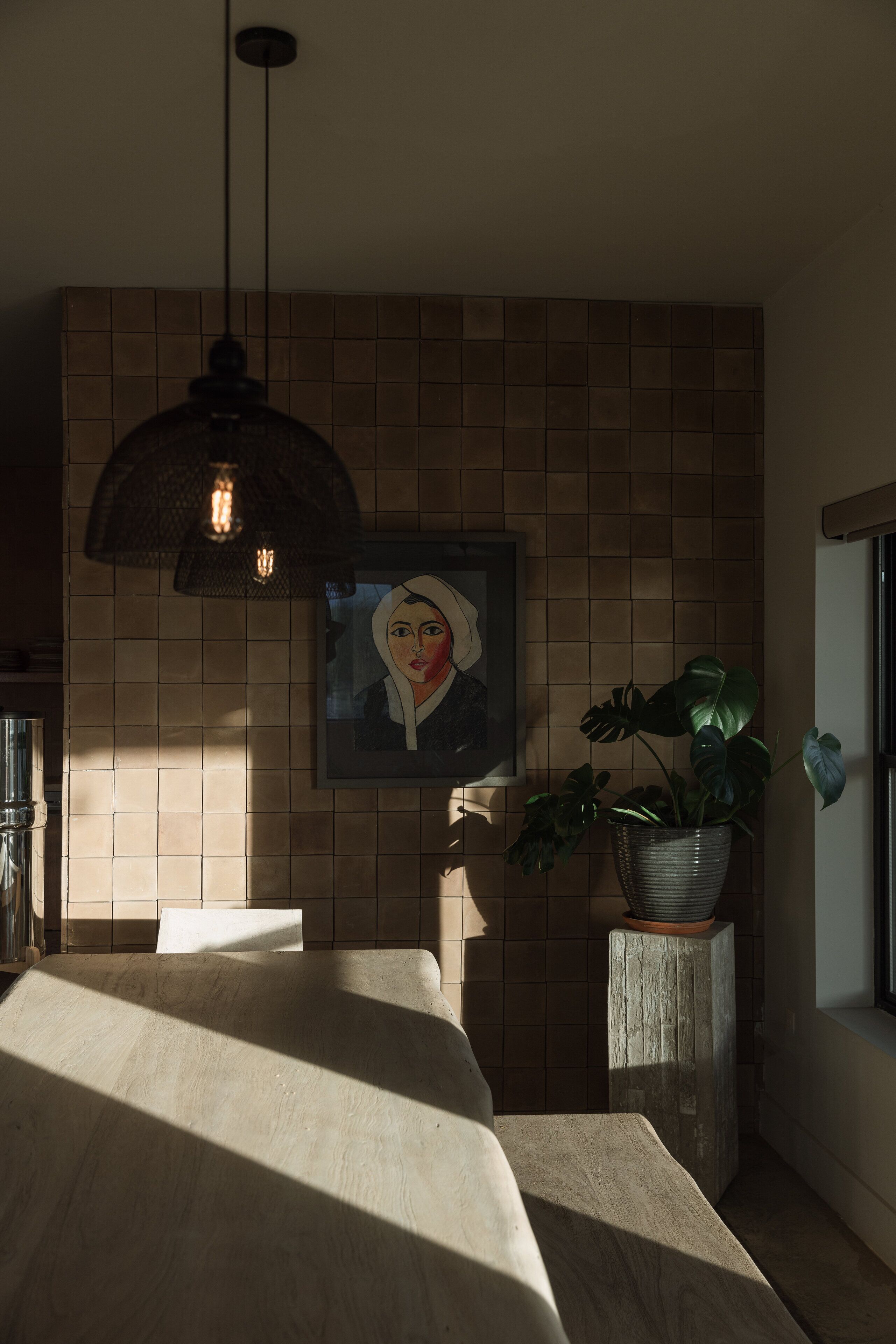 Een moderne keuken met een betegelde spatwand, hanglampen, een potplant en een lijstwerk aan de muur.