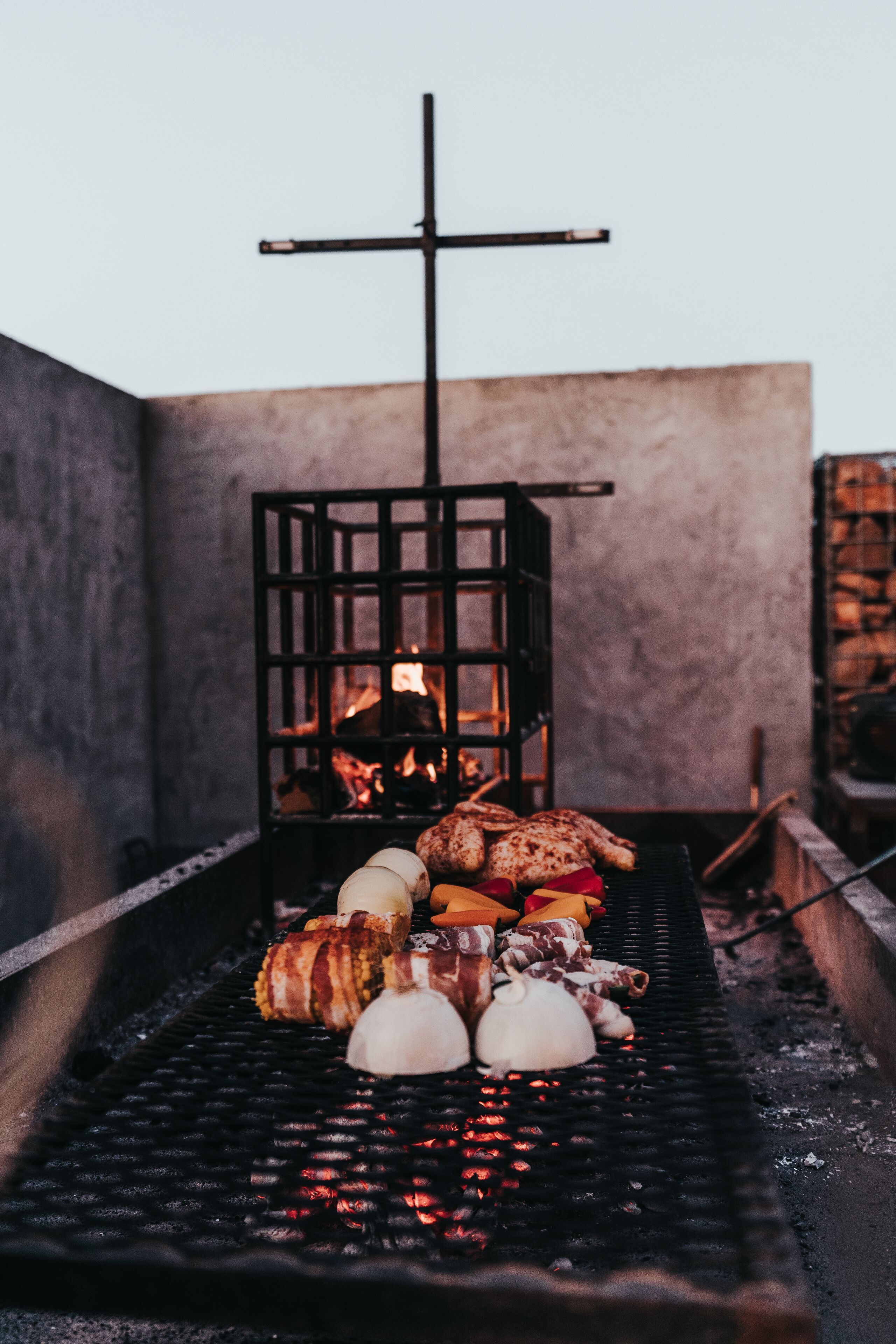 Una barbacoa amb diferents carns i verdures, una creu i un foc cremant al fons.
