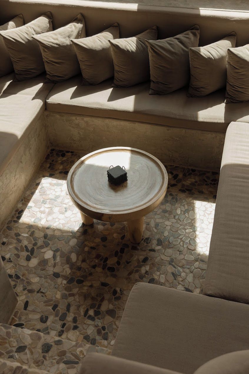 A sunlit outdoor seating area with a round table and cushions.