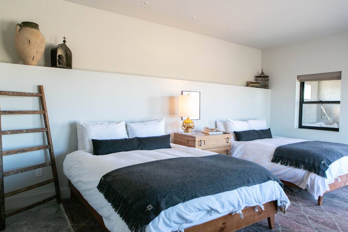 A bedroom with two beds, a wooden ladder, a nightstand, and a wall-mounted shelf with decorative items.
