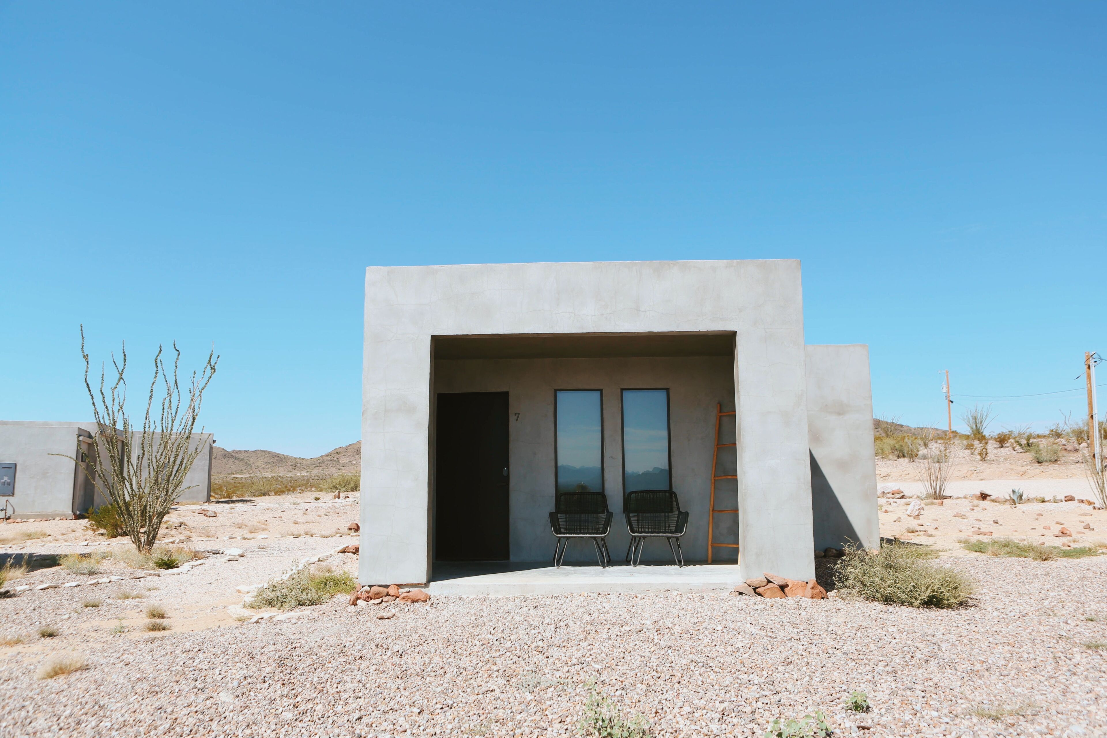 A modern building with a concrete facade, two black chairs outside, and a gravel ground.