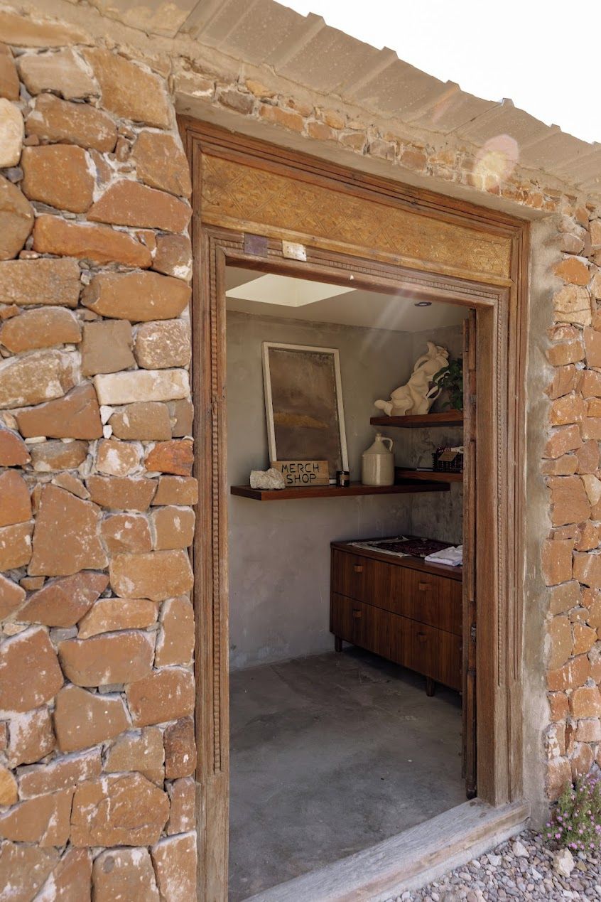 Un muro de piedra con una puerta de madera que da a un cuarto con un armario de madera y una repisa con objetos decorativos.