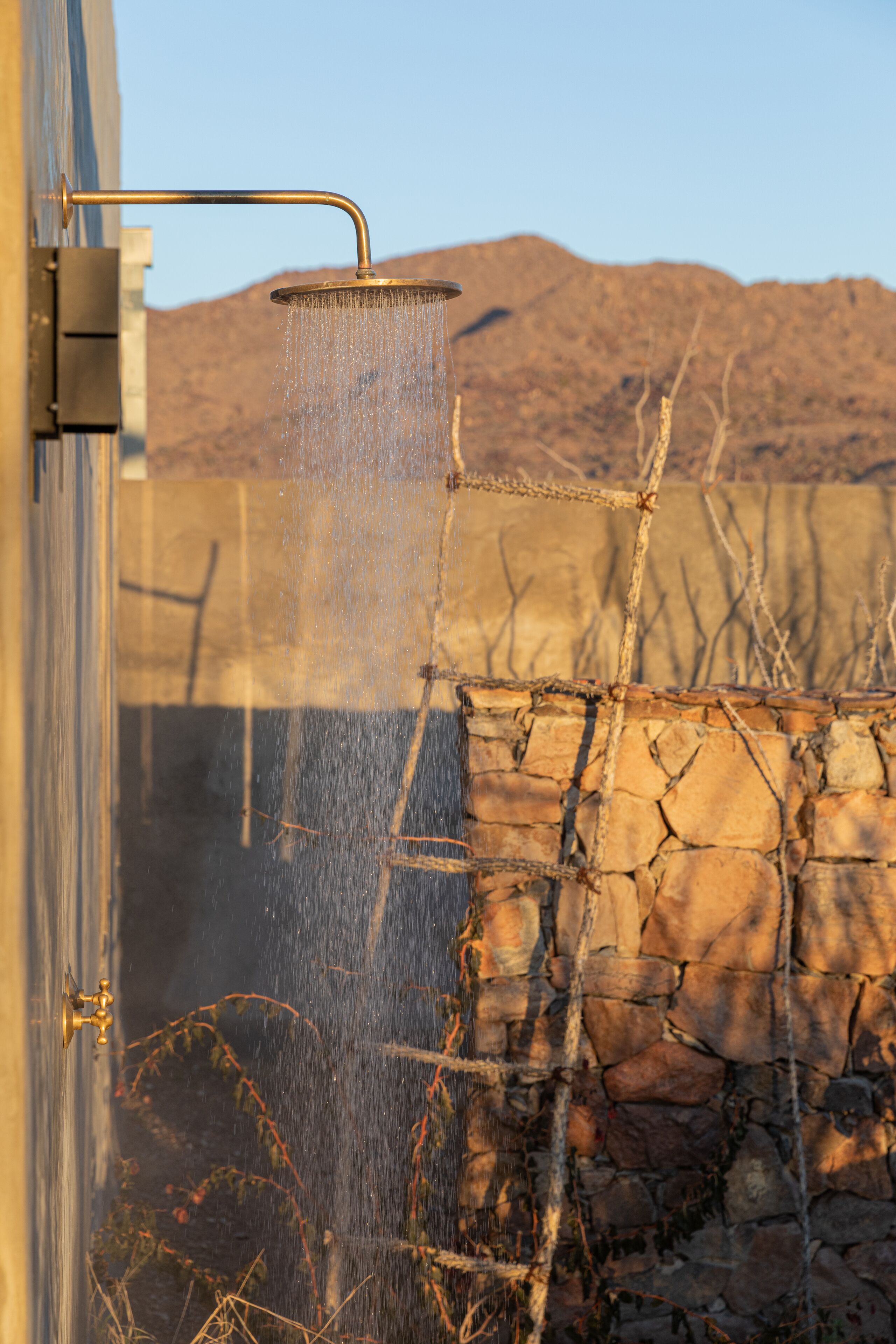 A showerhead with water flowing, a stone wall, and a mountain in the background.