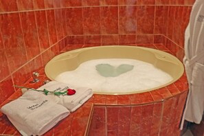 A bathtub with a heart-shaped foam design, a towel with a rose, and a small bottle on a marble-tiled floor. - Hotel Bohemia (Lima)