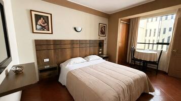 Habitación de hotel con cama, mesita de noche, una silla, una mesa y ventana con cortinas.