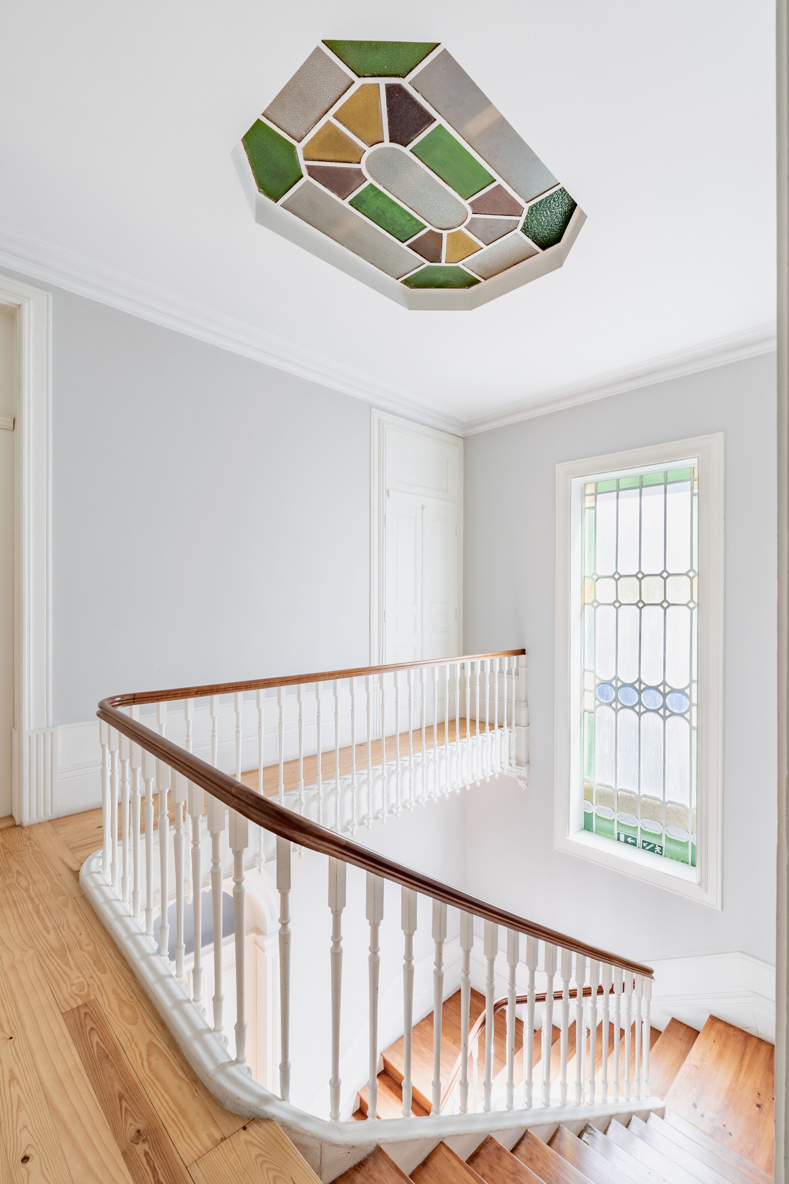 A staircase with white railings and wooden steps, leading to a landing with a stained glass ceiling.