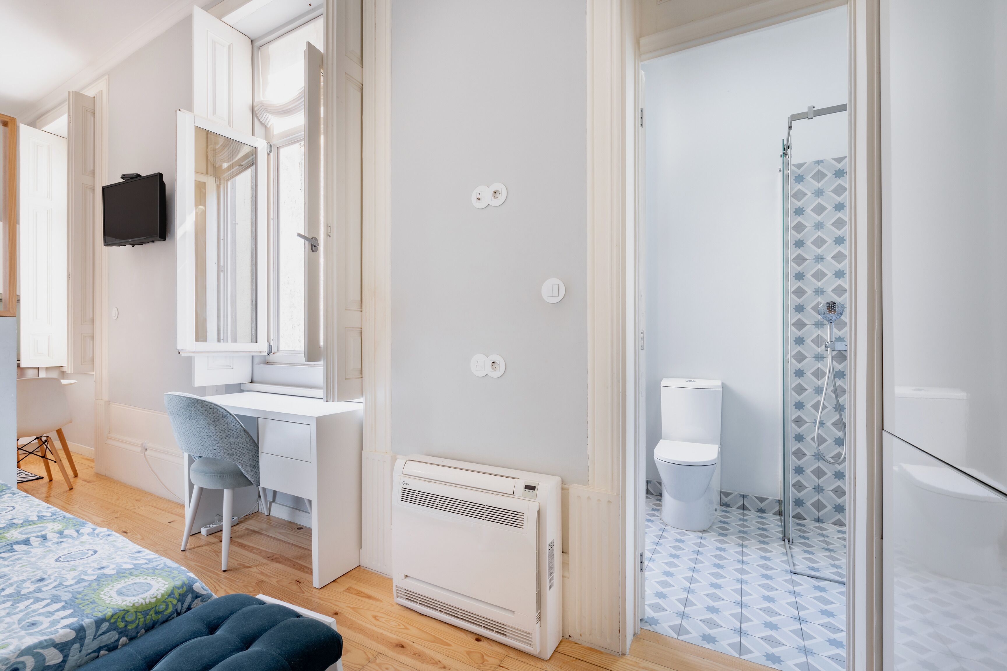 A modern hotel room with a desk, chair, and a shower area with patterned tiles.