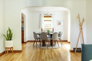 A dining area with a round table, six chairs, a potted plant, a hanging light fixture, and a framed picture on the wall.