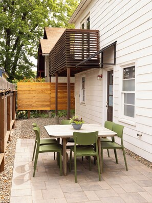 A patio with a wooden table and chairs, a small garden, and a wooden deck attached to a house.