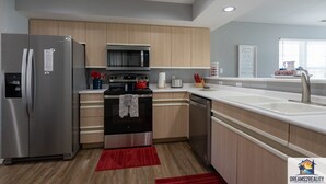 A modern kitchen with stainless steel appliances, wooden cabinets, and a red rug. - Fairways 11-3 (Branson)