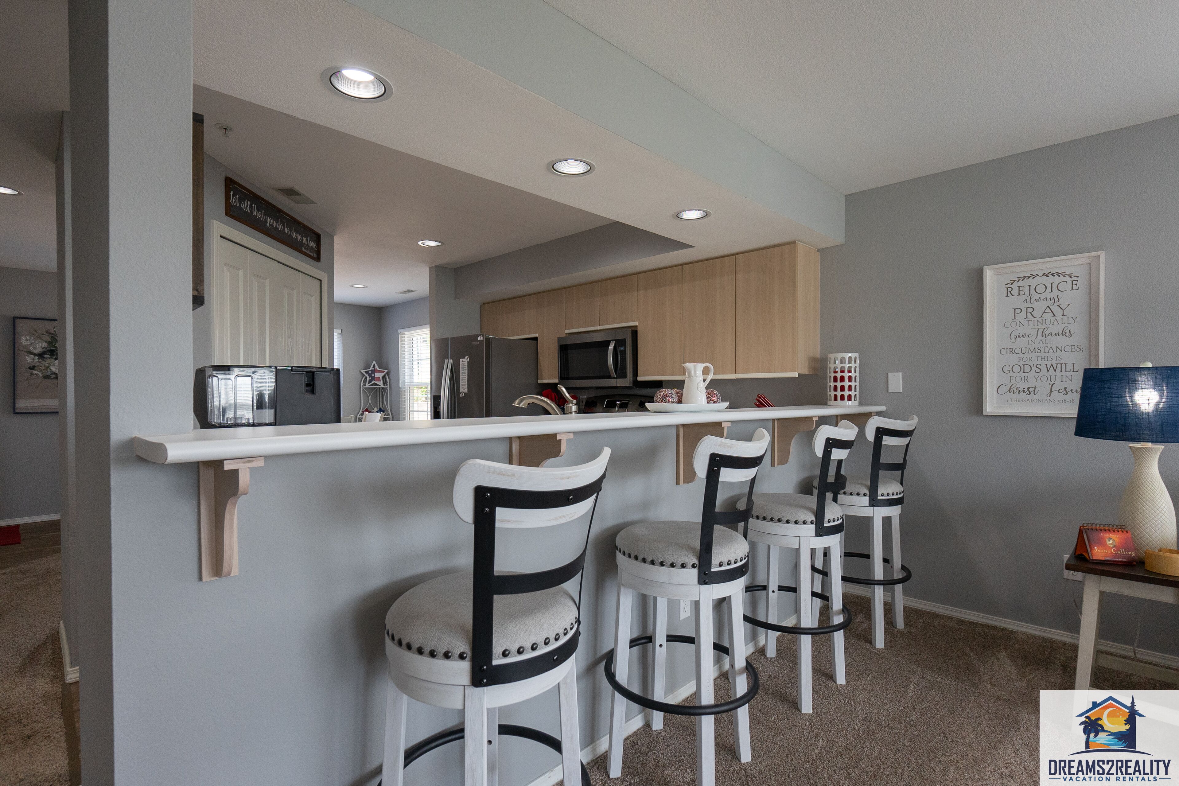Una cocina moderna con barra, taburetes blancos y microondas.