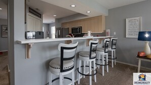 A modern kitchen with a bar area, white bar stools, and a microwave. - Fairways 11-3 (Branson)