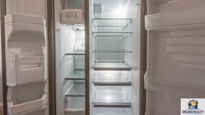 An interior of a modern, empty refrigerator with multiple shelves and a water dispenser. - Fairways 11-3 (Branson)