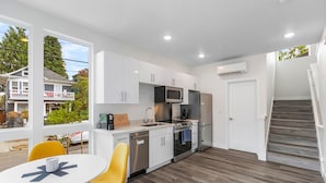 A modern kitchen with white cabinets, stainless steel appliances, and a dining area with yellow chairs. - Stag Sweet Suite (Seattle)