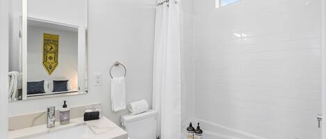 A modern bathroom with a white sink, toilet, and bathtub. There is a shower curtain, a towel rack, and two bottles of hand soap on the sink.