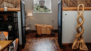 Habitación con bañera de madera, ventana con vista a árboles y una escultura de madera única.