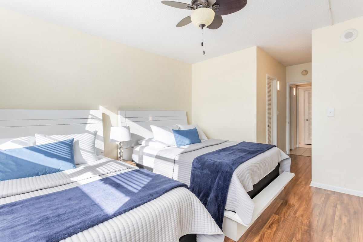 A bedroom with two beds, a ceiling fan, and a door leading to another room.