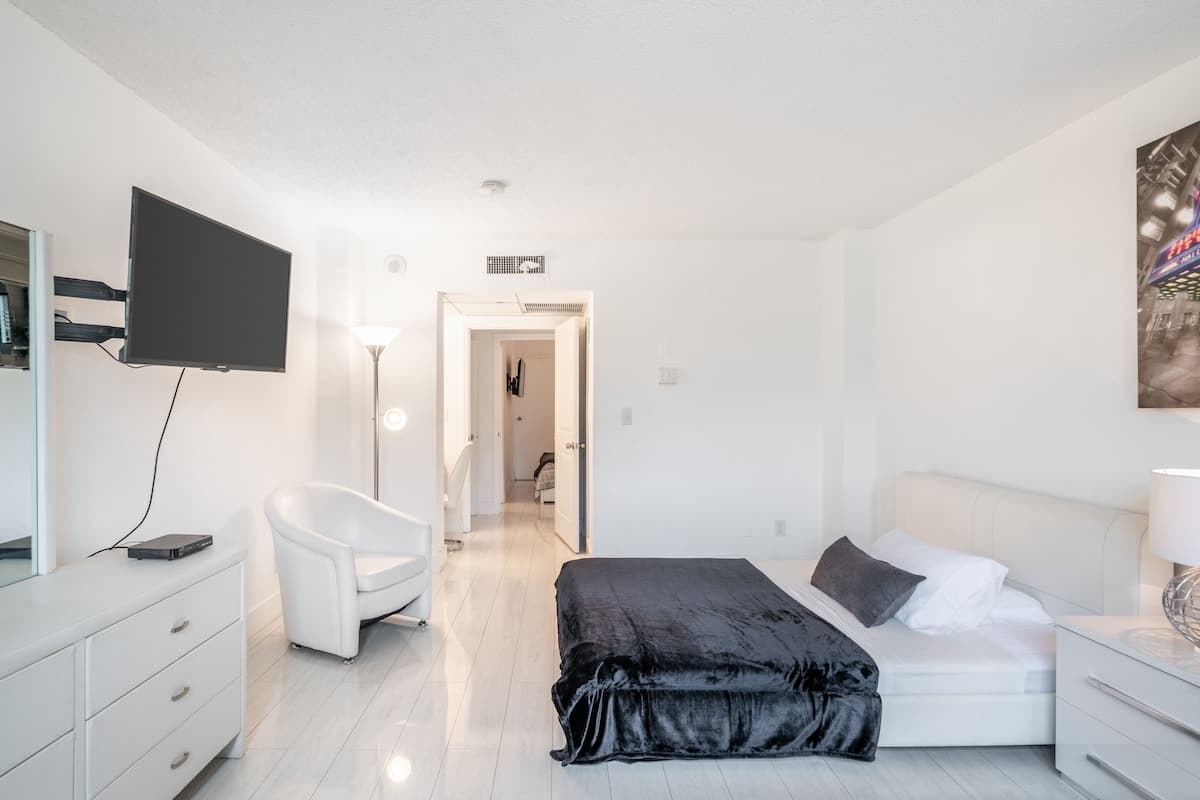 A modern bedroom with a bed, a chair, a TV, and a desk.