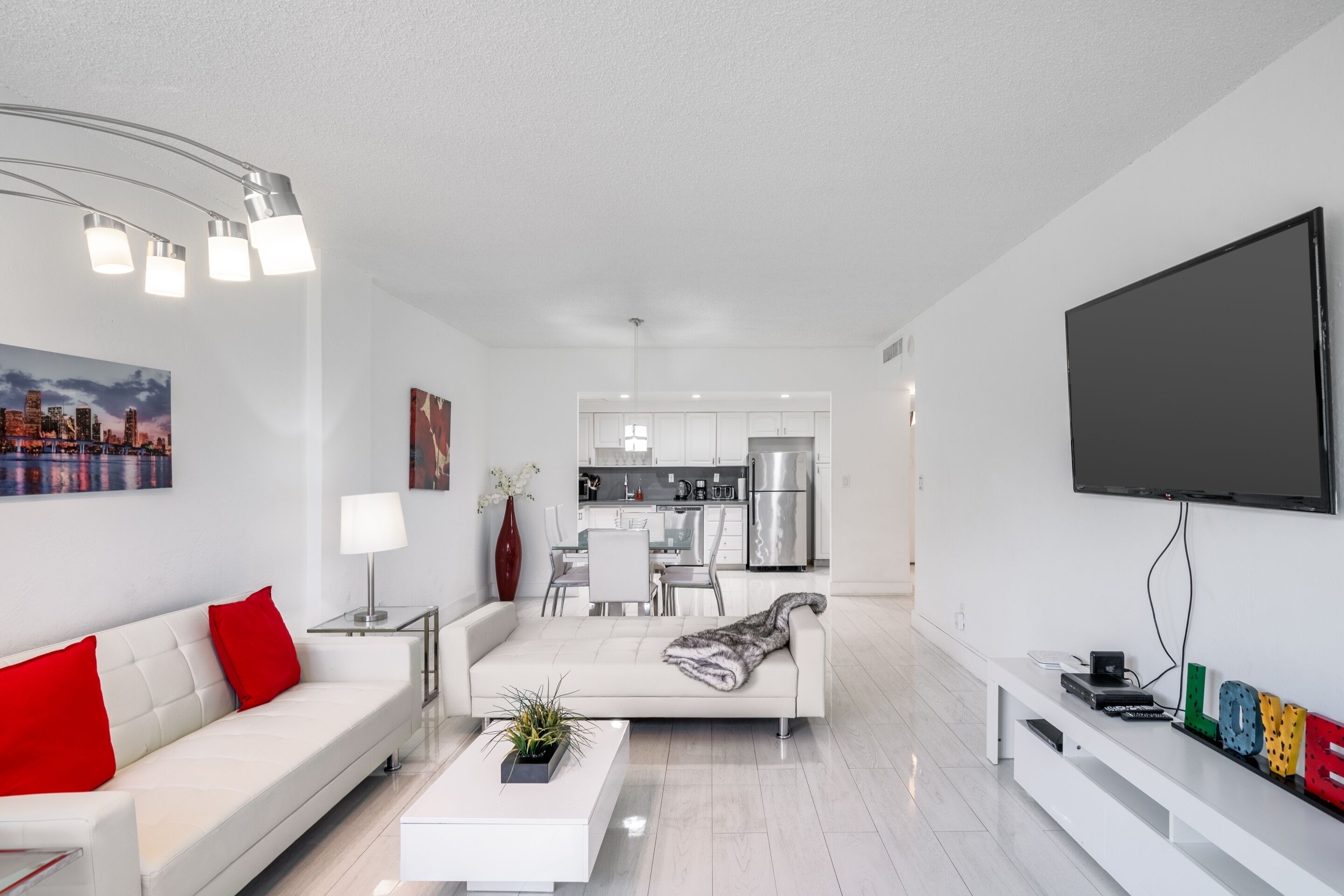 A modern living room with a sofa, coffee table, and TV. A kitchen is visible in the background.
