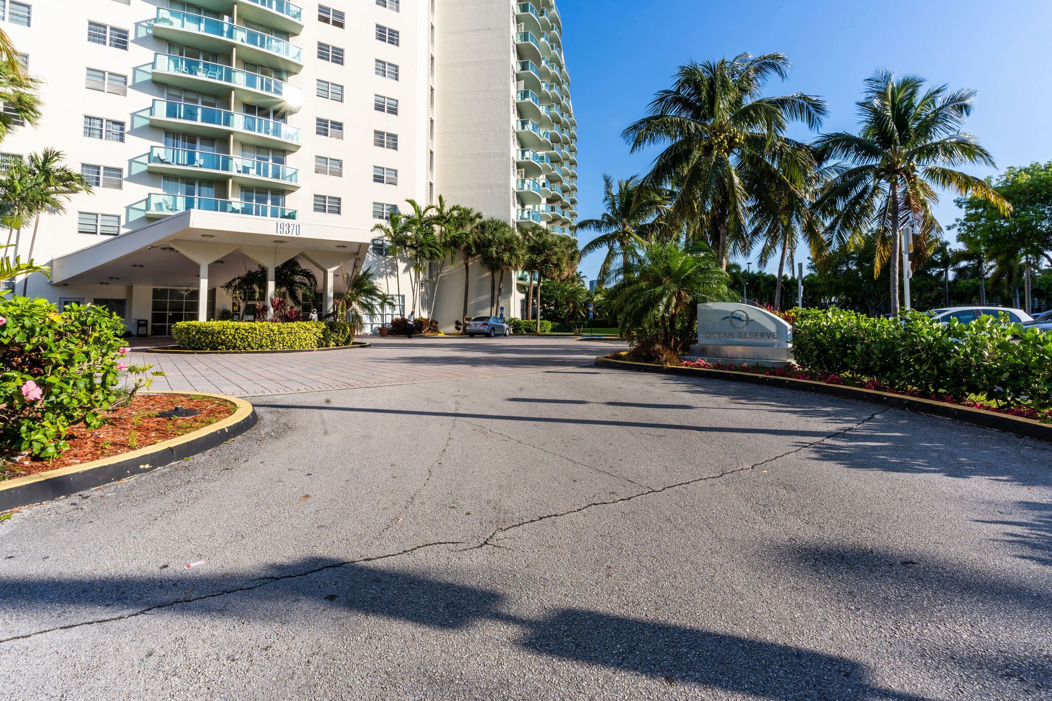 A hotel entrance with a modern design, palm trees, and a clear sky.