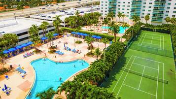 A hotel with a swimming pool, tennis courts, and a parking area.