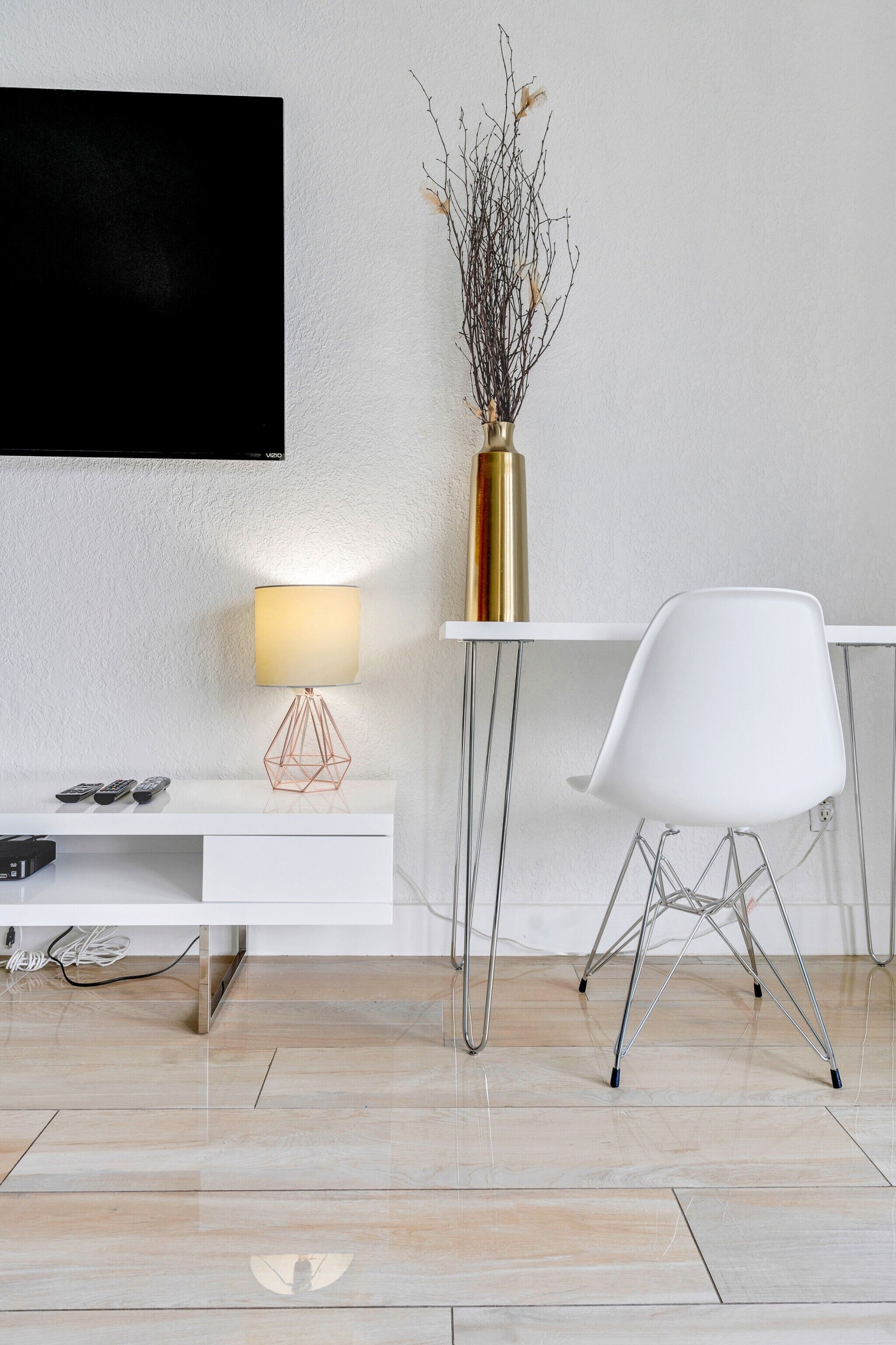 A modern living room with a white TV stand, a white chair, a lamp, and a vase with branches.