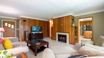 A living room with a fireplace, a television, and a kitchen area visible through an open doorway.