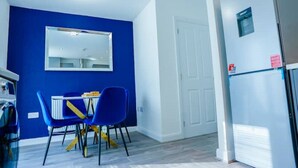 A compact kitchen with a blue wall, a white door, and a refrigerator. - Cosy 3 Bedroom House Set In Manchester Free wifi & private parking (Greater Manchester)