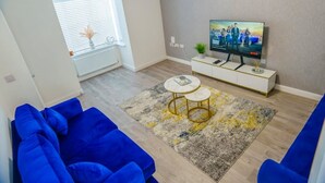 A living room with a blue sofa set, a TV on a white cabinet, and a patterned rug. - Cosy 3 Bedroom House Set In Manchester Free wifi & private parking (Greater Manchester)