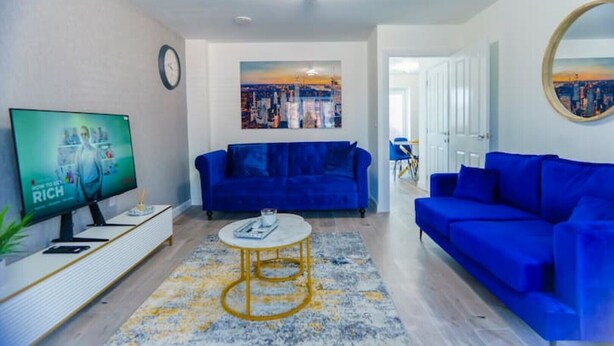 A living room with a blue sofa, a coffee table, a TV, and a painting on the wall. - Cosy 3 Bedroom House Set In Manchester Free wifi & private parking (Greater Manchester)