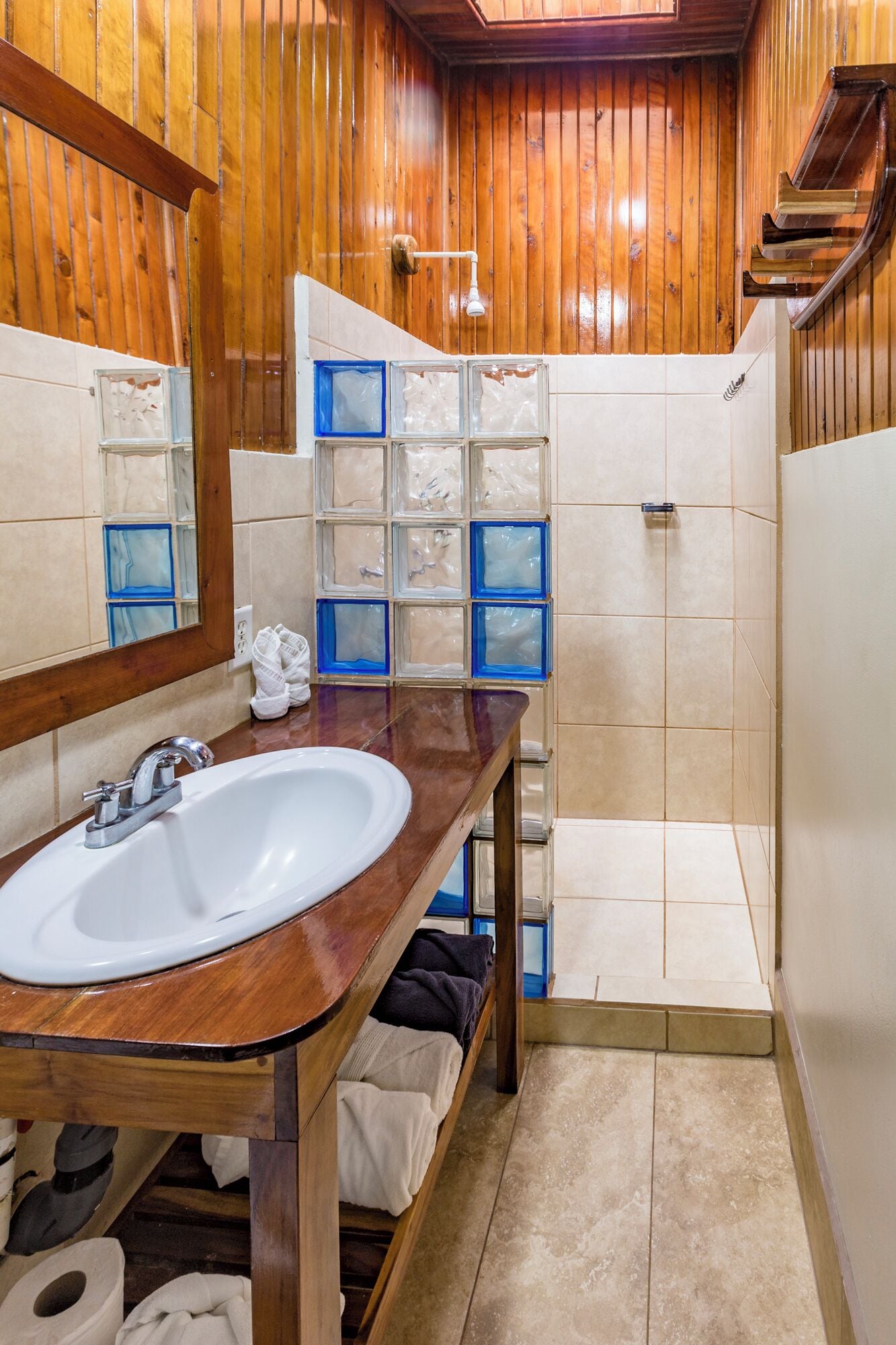 A wooden bathroom with a sink, mirror, and tiled shower.