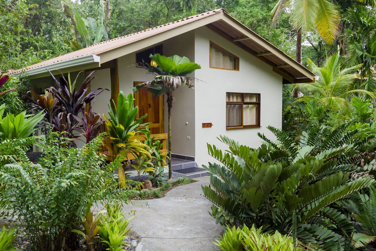 A two-story house with a sloped roof, surrounded by lush tropical vegetation.