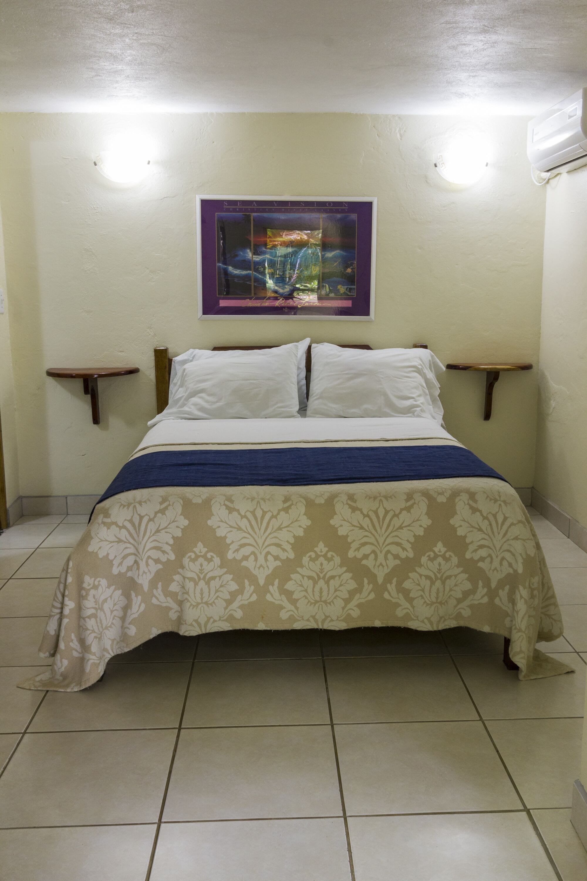 Un lit recouvert d’une couvre-lit à motifs floraux, deux tables de chevet et un cadre photo fixé au mur.