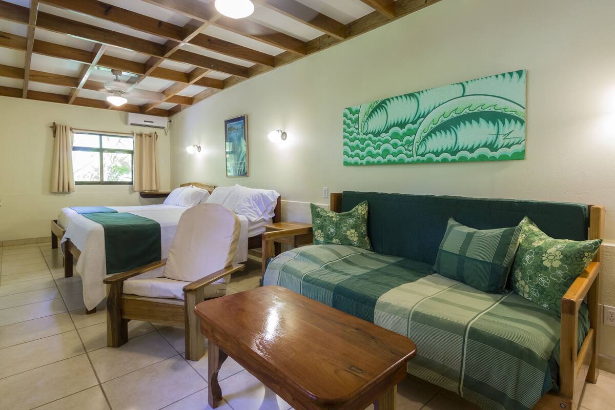 A room with a bed, a sofa, a wooden table, and a wall-mounted air conditioner.