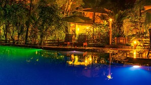A nighttime pool area with lounge chairs and umbrellas, surrounded by lush vegetation. - LA PONDEROSA Beach & Jungle Resort (Pavón)
