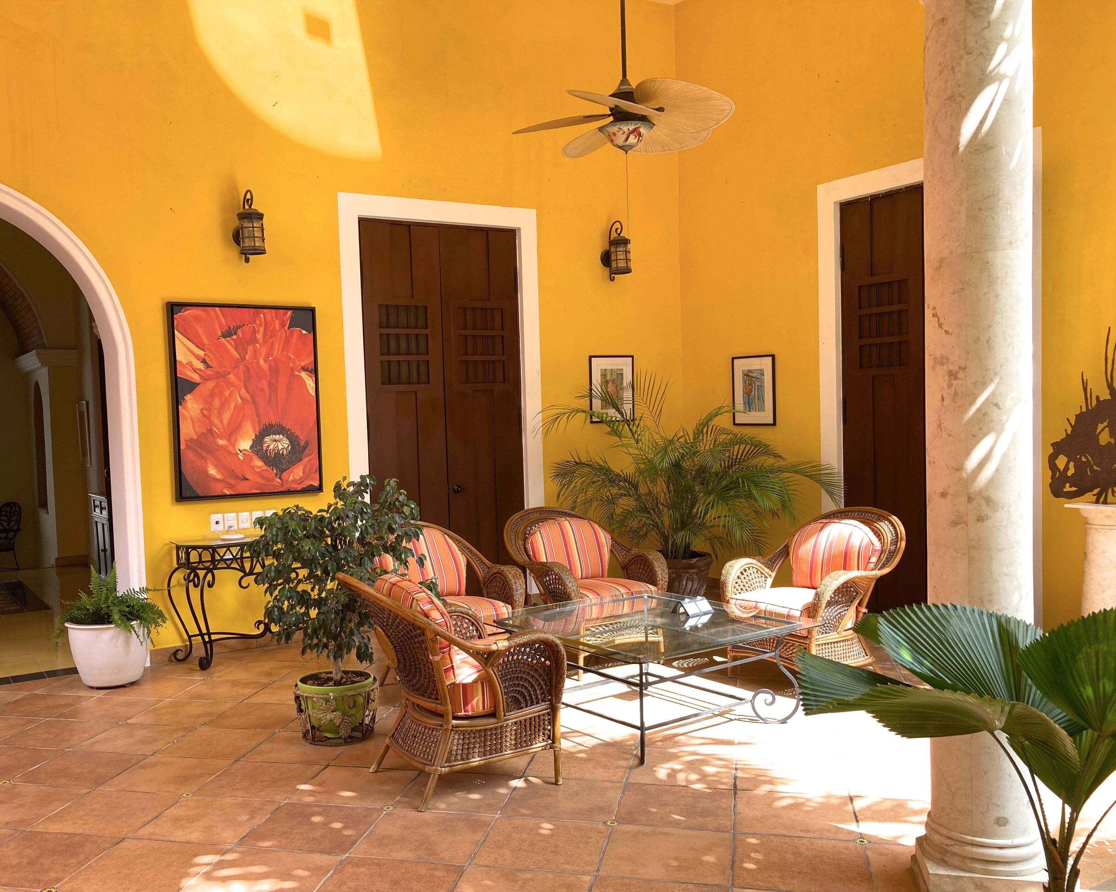 A sunlit patio with wicker furniture, a glass table, and potted plants.