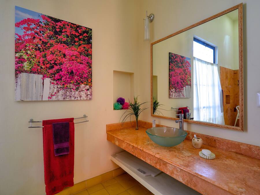 Un baño con un lavamanos de mármol, un espejo grande y un cuadro de flores rosas.