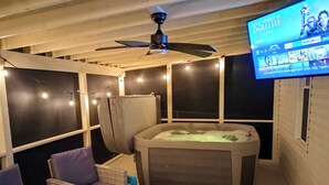 Un espace extérieur accueillant avec des sièges confortables, un jacuzzi, des guirlandes lumineuses et un écran de télévision diffusant un film.